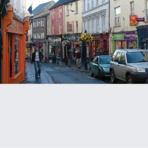 A narrow street lined with colorful buildings and parked cars.
