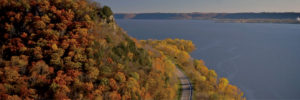 Scenic autumn landscape with a railway track along a colorful forest and calm lake.